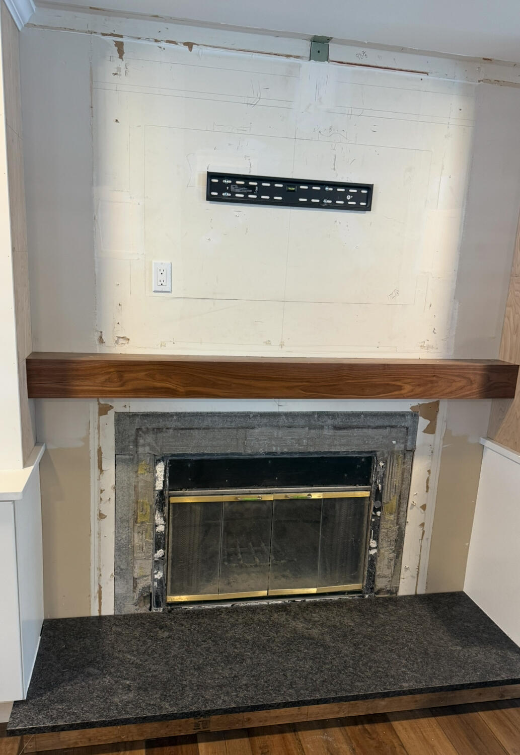 Fireplace before renovation with plain wall and wood mantel