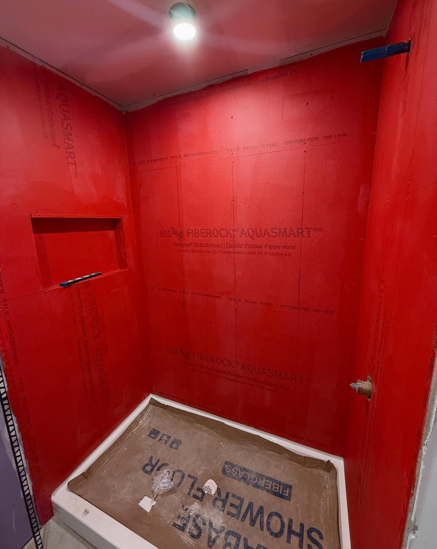 Shower renovation in progress with red waterproofed walls and recessed niche Shower renovation in progress with red waterproofed walls and recessed niche