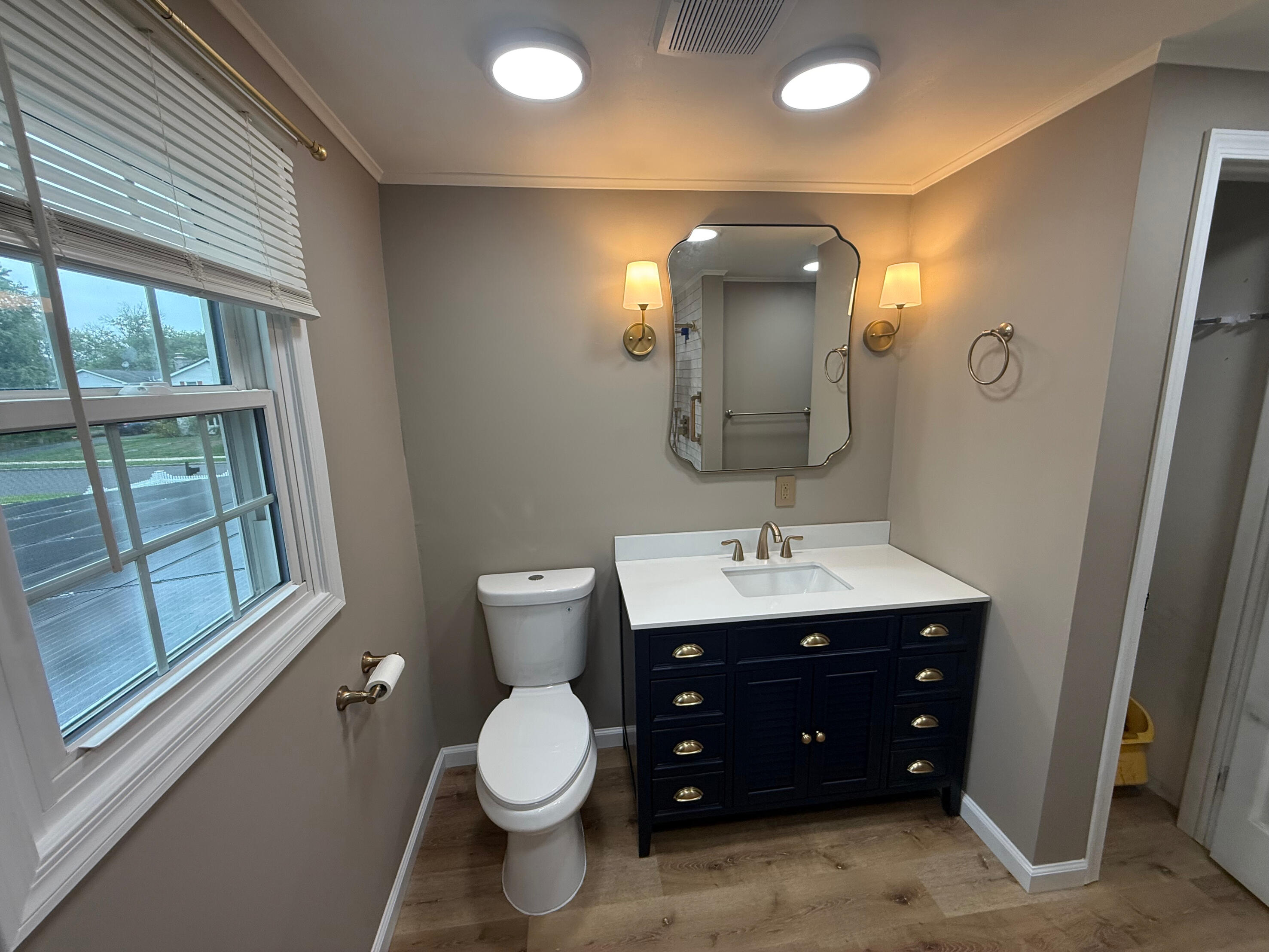 JLC Kitchen & Bath Remodeling Remodeled bathroom with navy vanity, white countertop and brass wall lights
