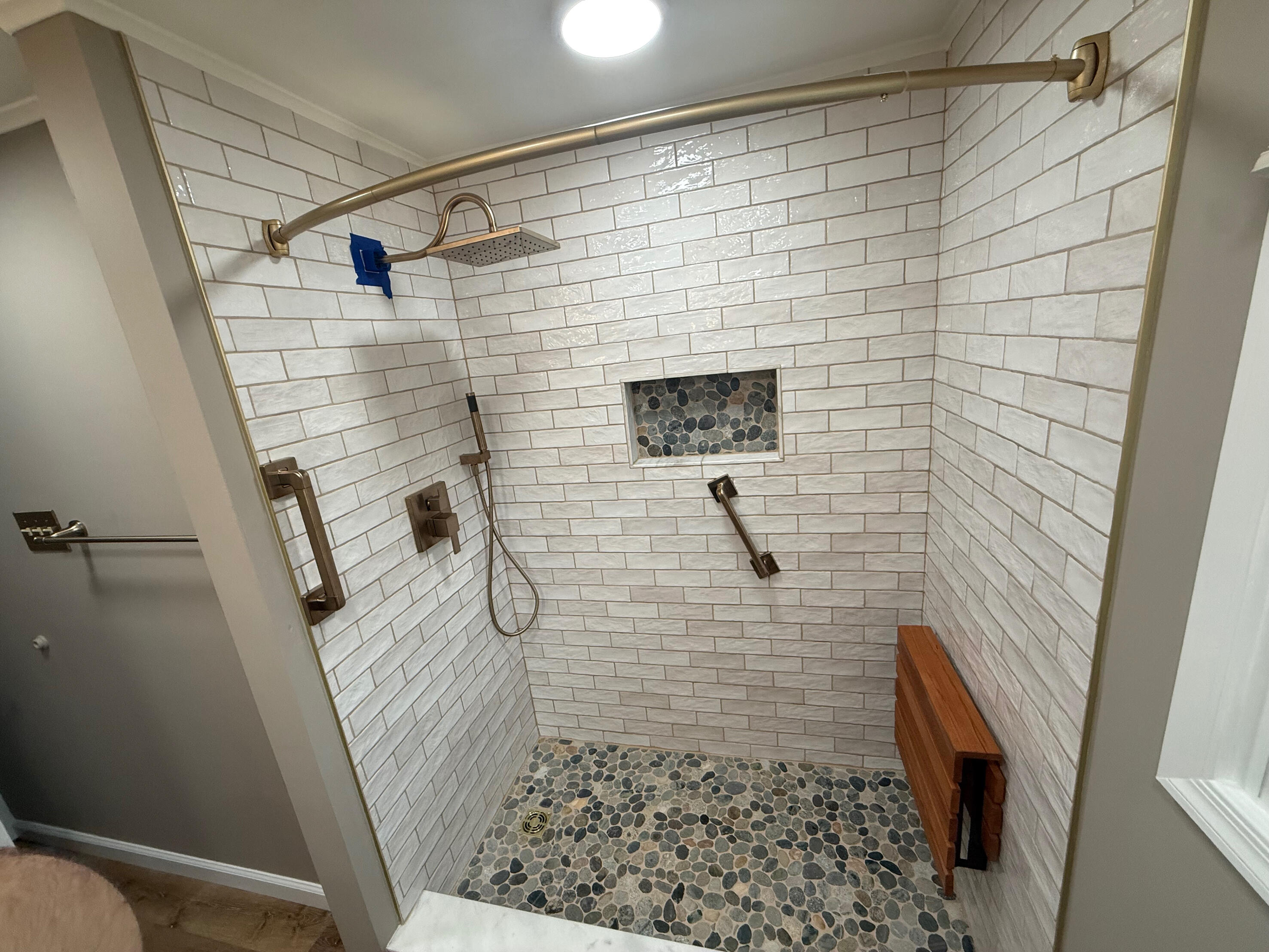 White tiled walk-in shower with pebble floor, recessed niche and grab bars